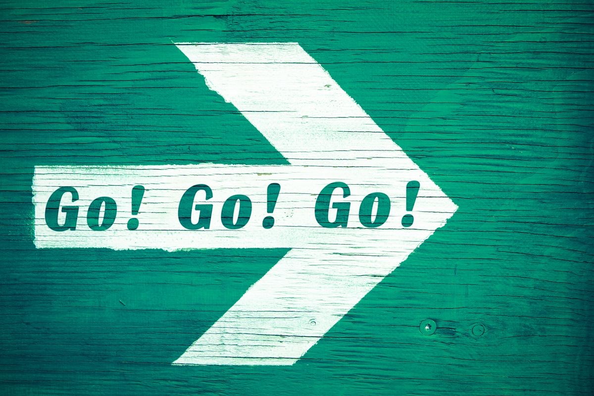 "Go! Go! Go!” motivational text written on a white directional arrow pointing towards right painted on a green blueish wooden signboard background. Photo with vignetting and green toned.